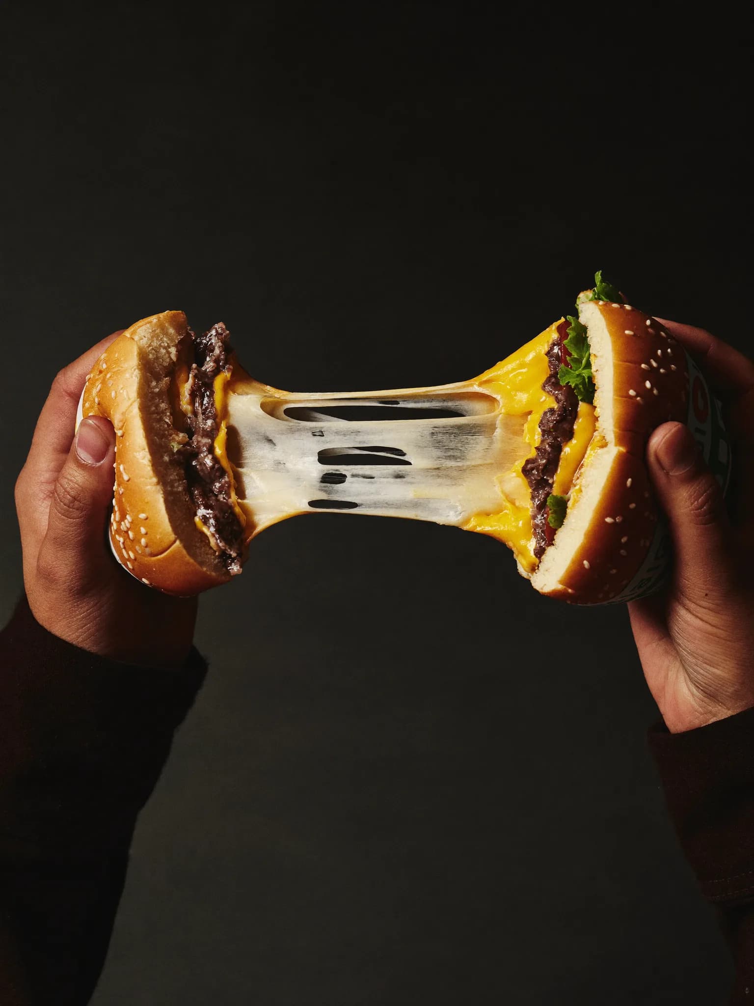 Burger halves pulled apart with a long stretchy melted cheddar cheese pull