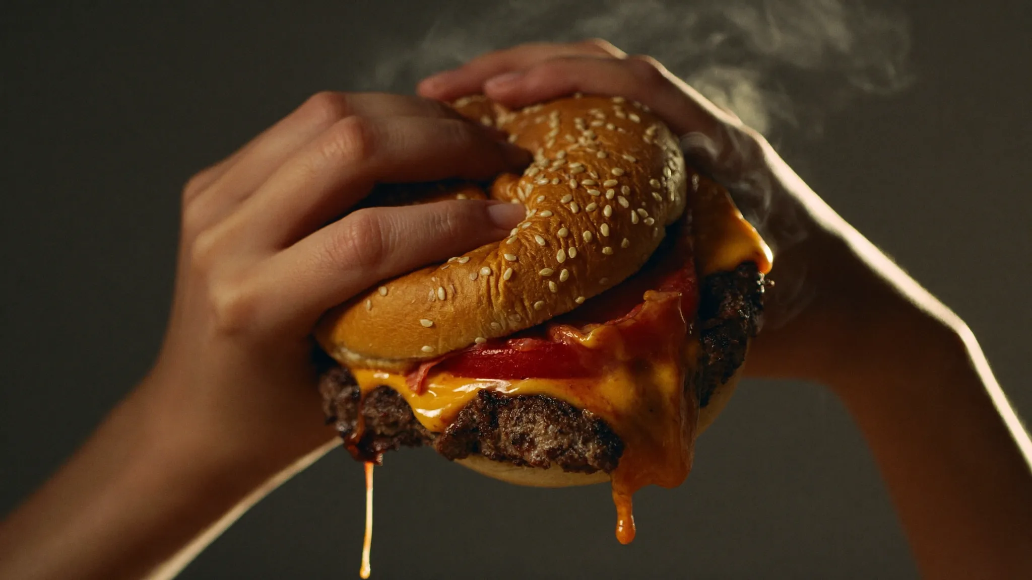 Hands lifting a dripping smashed cheeseburger toward a first bite